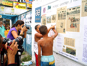 Crianças apontam as marcas de tiros feitas no Mural Contra a Viol~encia da comunidade Nova Holanda